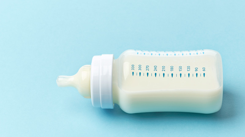 Grande plano de biberão com leite, deitado sobre uma mesa azul clara